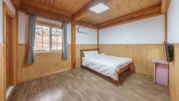 A bedroom with wooden paneling, a bed, a window with curtains, and a flat-screen TV mounted on the wall.