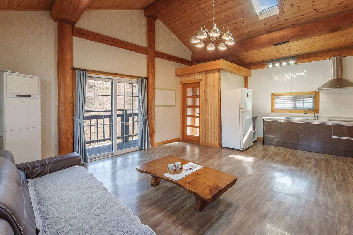 Una sala de estar acogedora con sofá, una mesa de centro de madera y una zona de cocina con refrigerador, lavamanos y armarios.