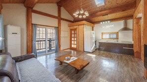 A cozy living room with a sofa, a wooden coffee table, and a kitchen area with a refrigerator, sink, and cabinets. - Daecheon Ocean Forest Pension (Boryeong)