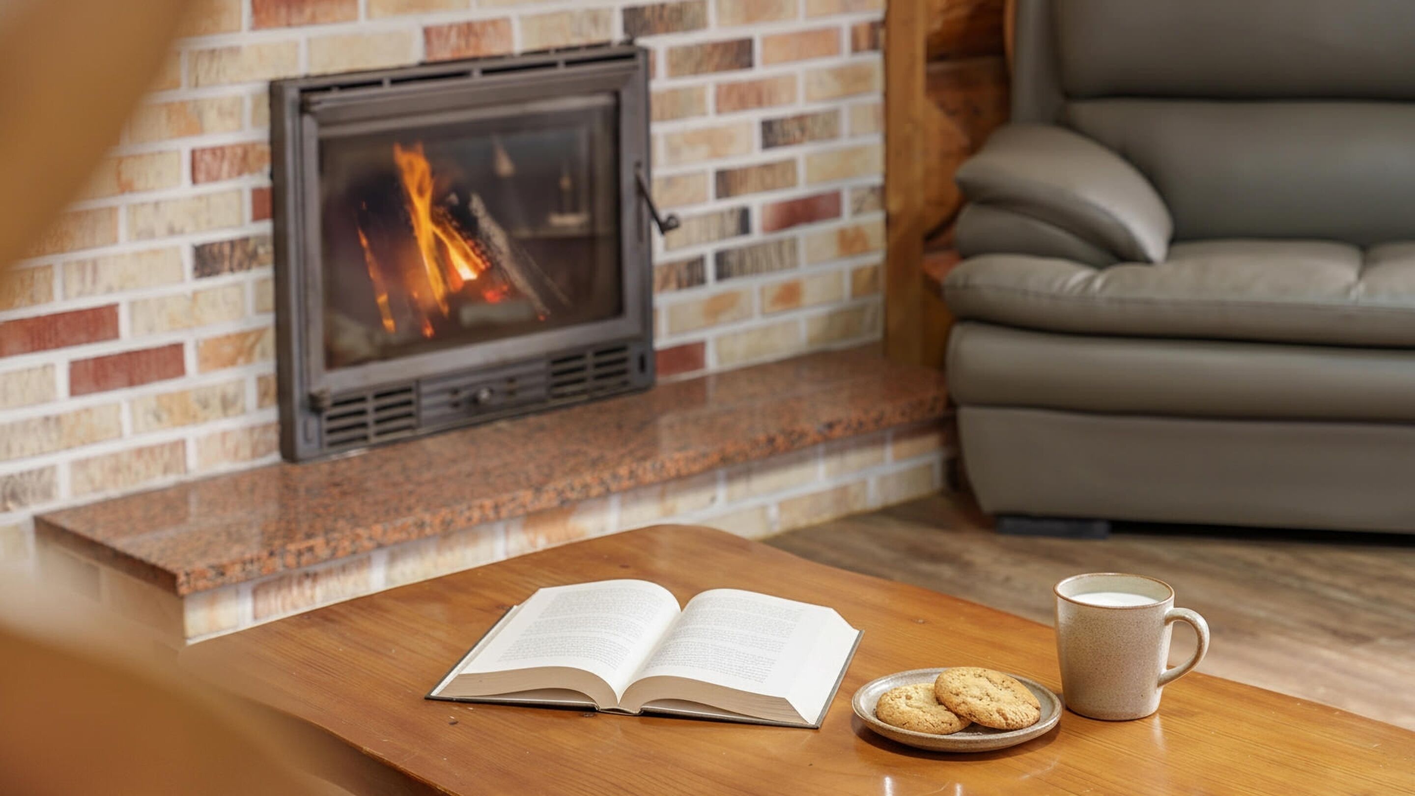 A cozy living room with a fireplace, a sofa, a coffee table with an open book, cookies, and a mug.