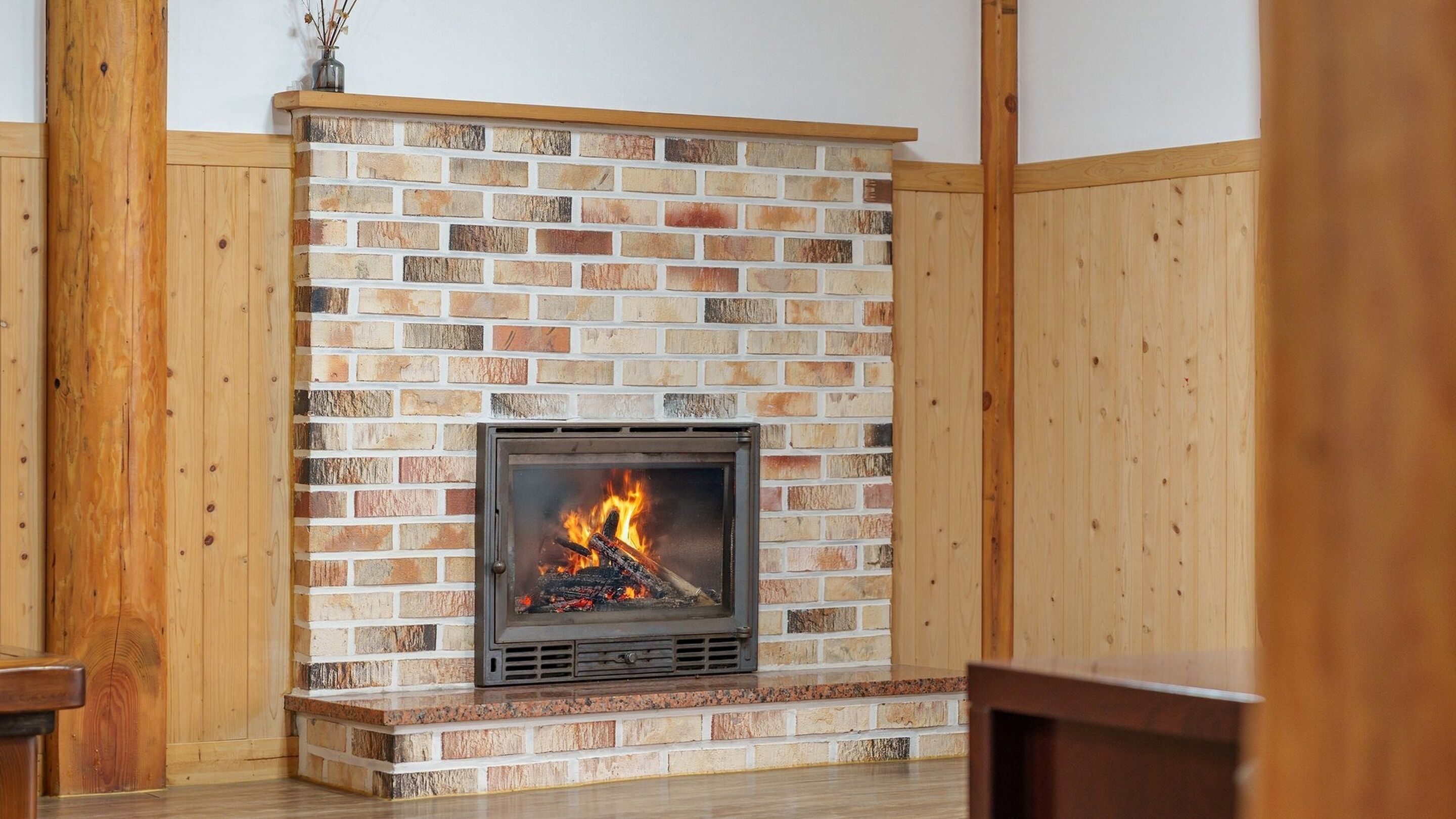 A fireplace with a brick wall, wooden paneling, and a fire burning inside.