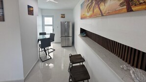 A modern kitchen with a stainless steel refrigerator, a dining table with chairs, and a wall-mounted shelf with decorative items. - Villa Tropicana  (Carolina)