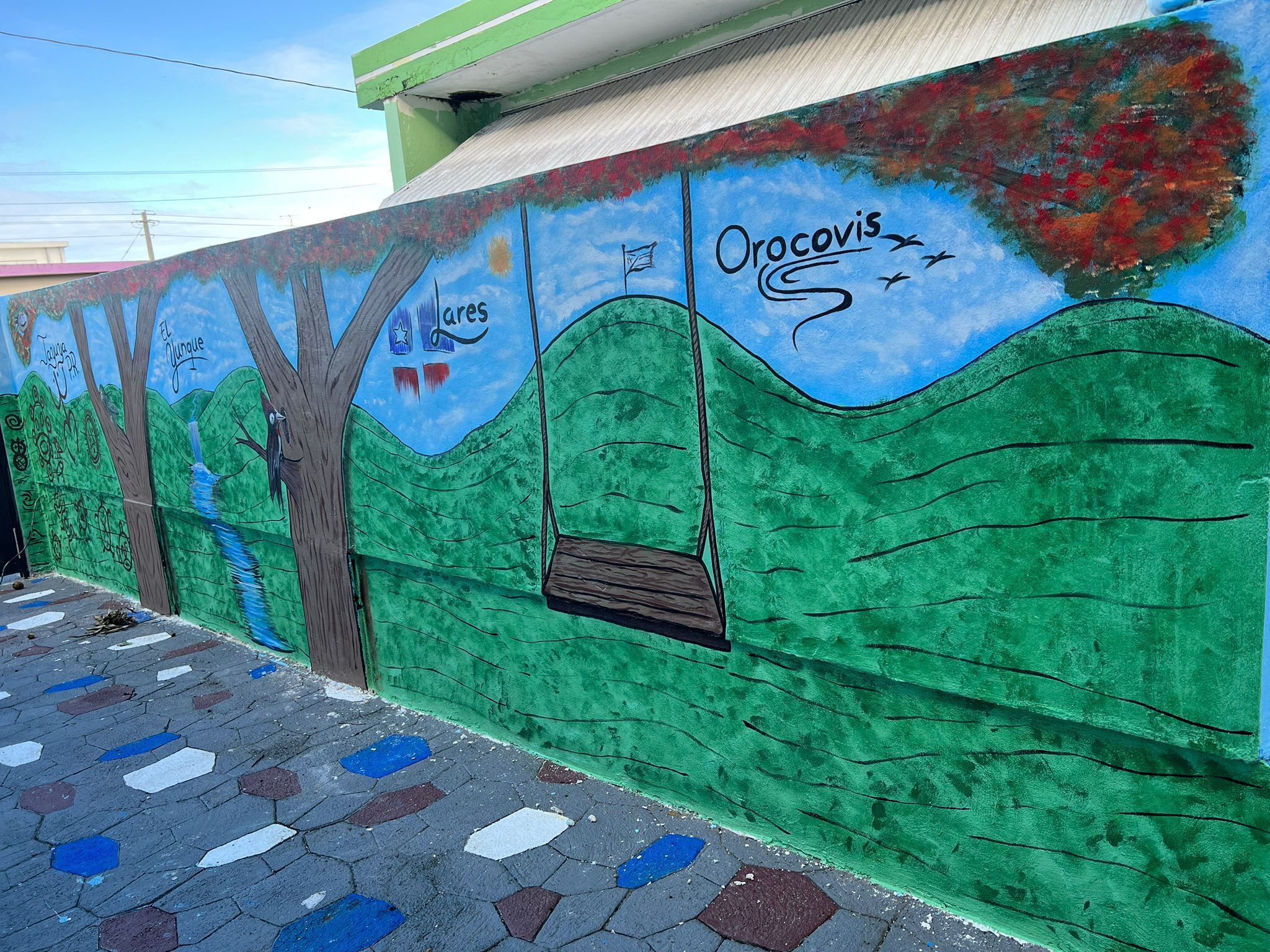 Et vægmaleri med et træ, en gyngestol og ordet "Orocovis".