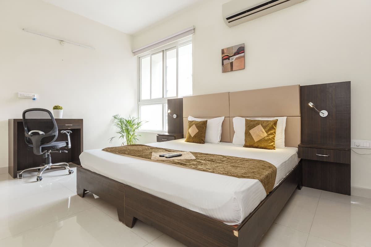 Una habitación de hotel moderna con una cama grande, un escritorio, una silla, una planta en maceta y una ventana.