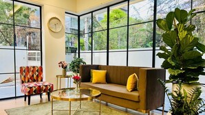 A modern living room with a sofa, armchair, coffee table, and large windows. - Olive Serviced Apartments Hitech City Hyderabad (Hyderabad)
