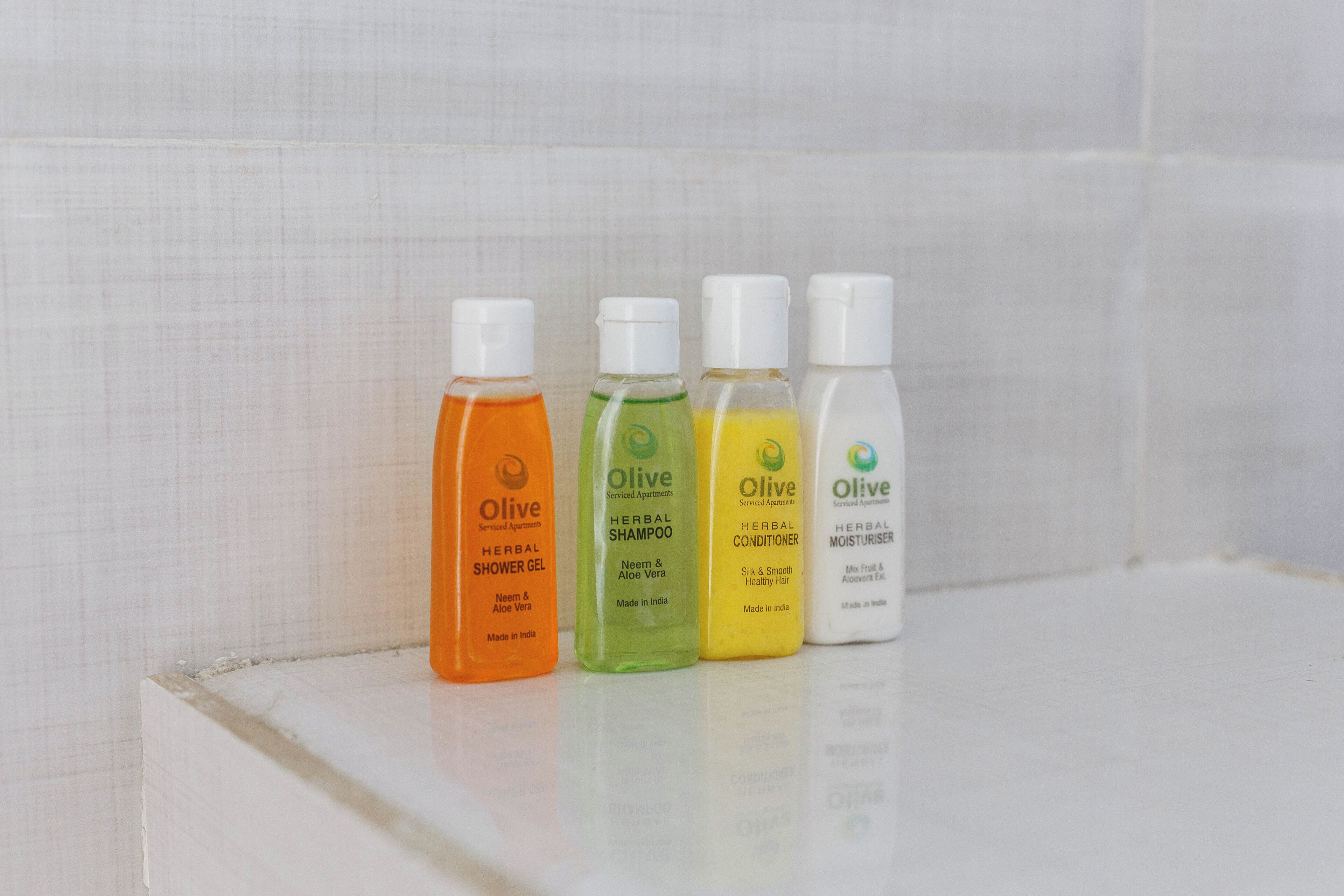 Vier Flaschen Produkte der Marke Olive auf weißer Oberfläche.