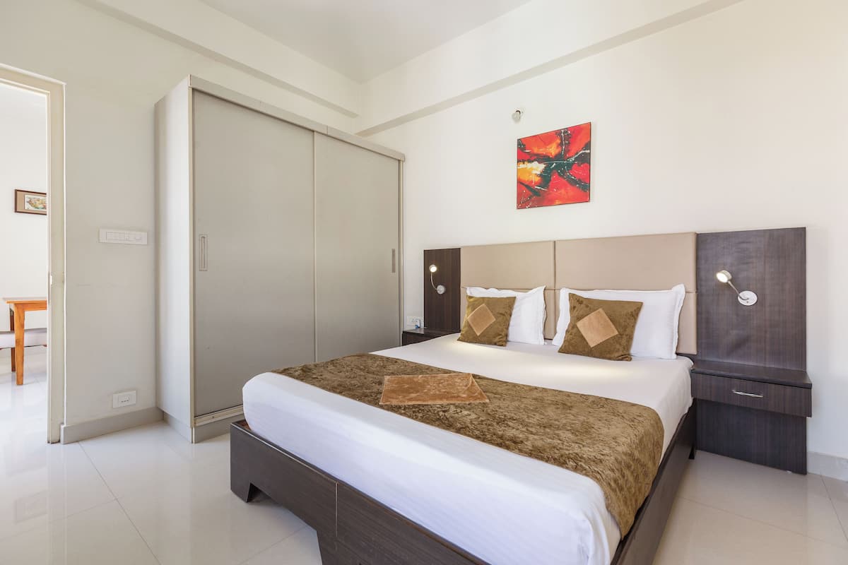 Una habitación de hotel con cama, armario, mesita de noche y un cuadro en la pared.