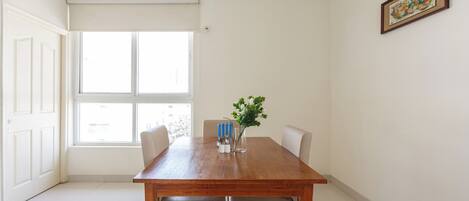 A dining area with a wooden table, four chairs, a vase with a plant, and a window with blinds.