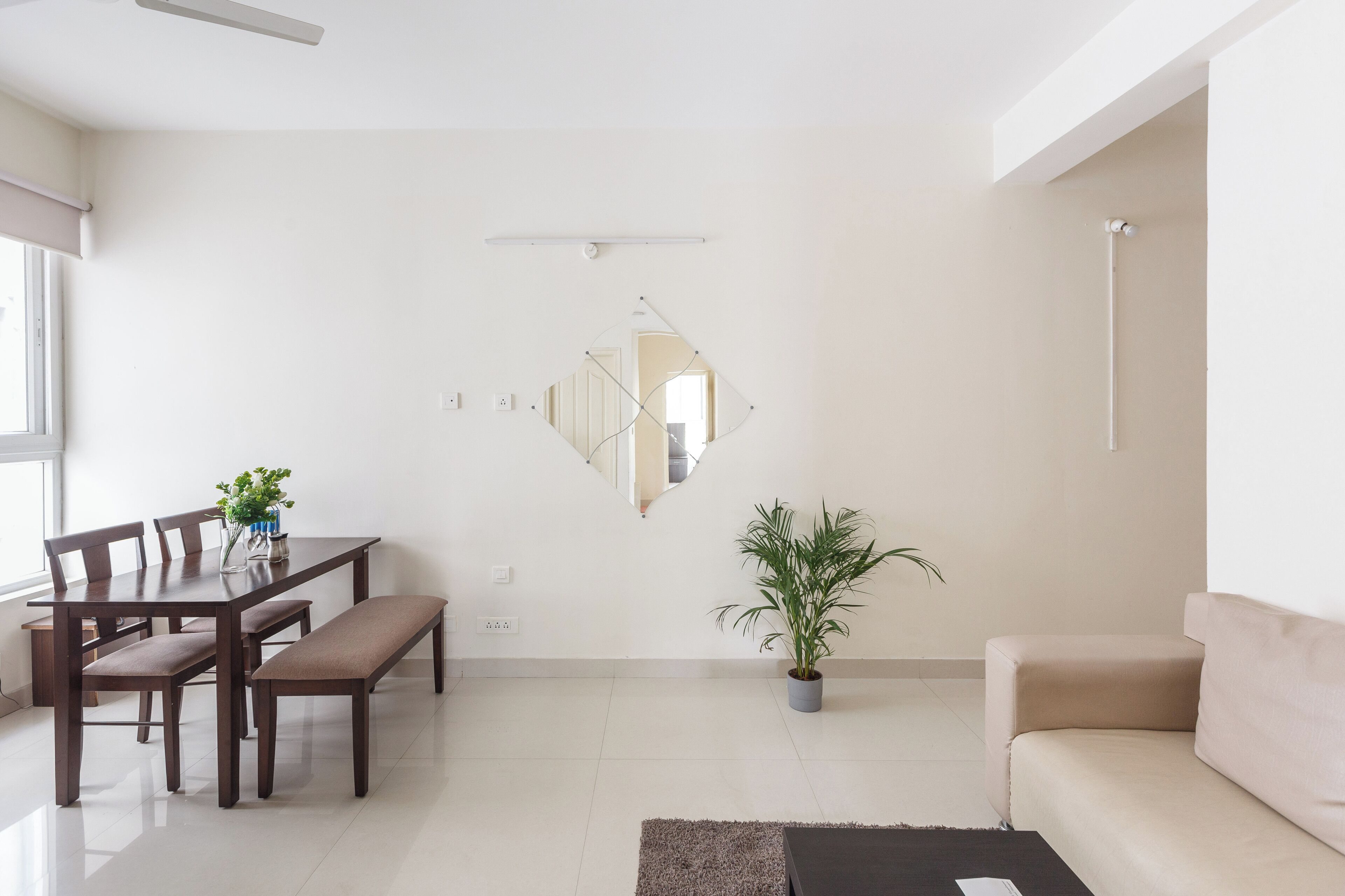 Una sala de estar moderna con una mesa de comedor, bancos, un sofá, una planta en maceta y un espejo en la pared.
