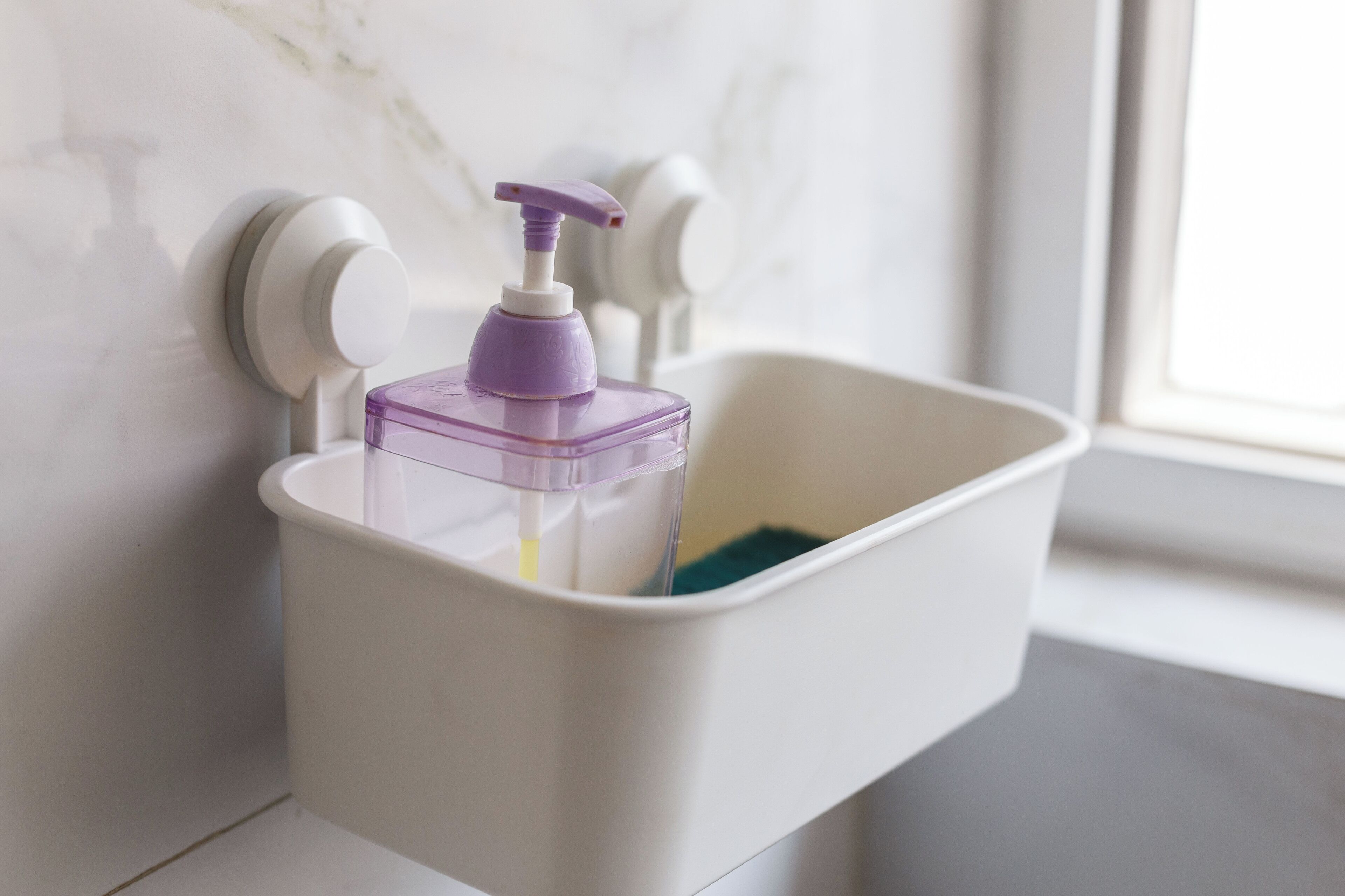 A bathroom with a white sink, a purple soap dispenser, and a white trash bin.