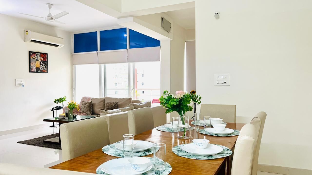 Zona pranzo moderna con tavolo in legno apparecchiato per quattro persone, una poltrona in fondo e un'ampia finestra vista edifici.