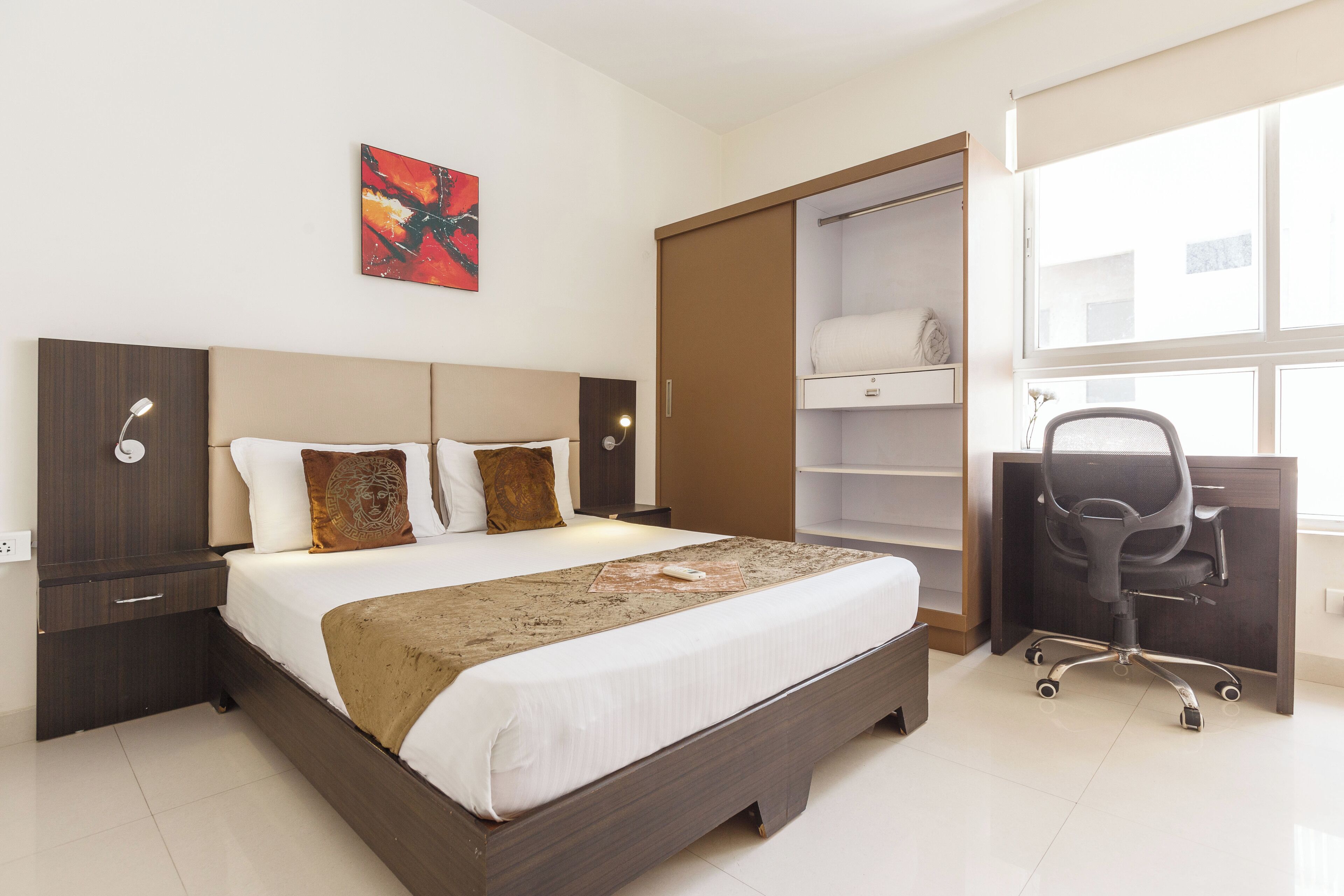Une chambre d’hôtel avec un lit, un bureau, une chaise, une armoire et une fenêtre.