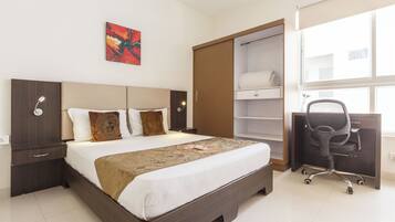 Une chambre d’hôtel avec un lit, un bureau, une chaise, une armoire et une fenêtre.