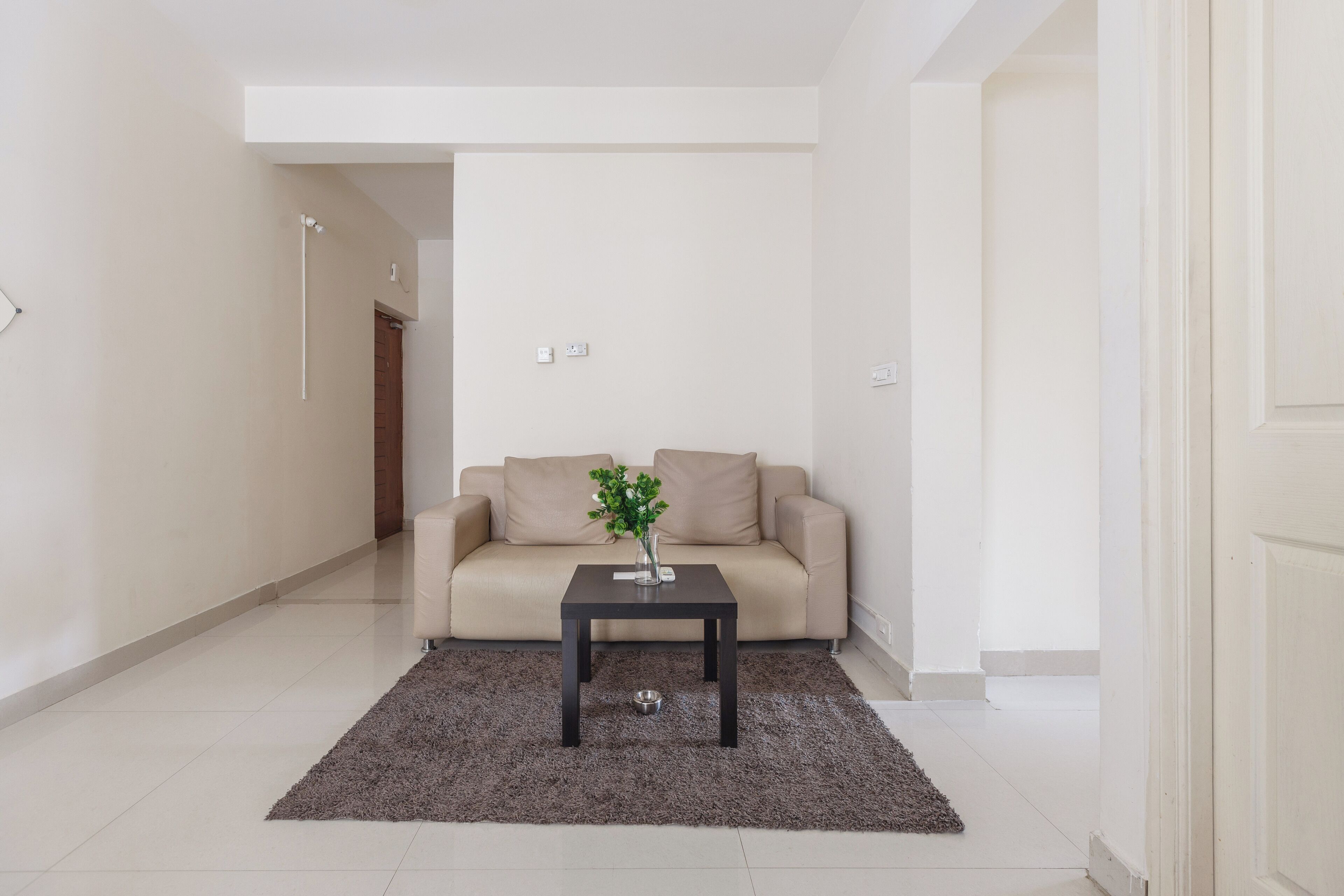 Una sala moderna con un sofá beige, una mesa de centro de madera oscura y una planta pequeña.