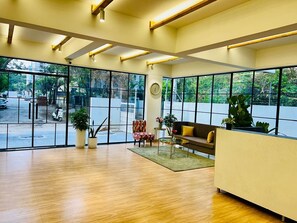 A spacious room with large windows, a sofa, a chair, and a small table. - Olive Serviced Apartments Hitech City Hyderabad (Hyderabad)