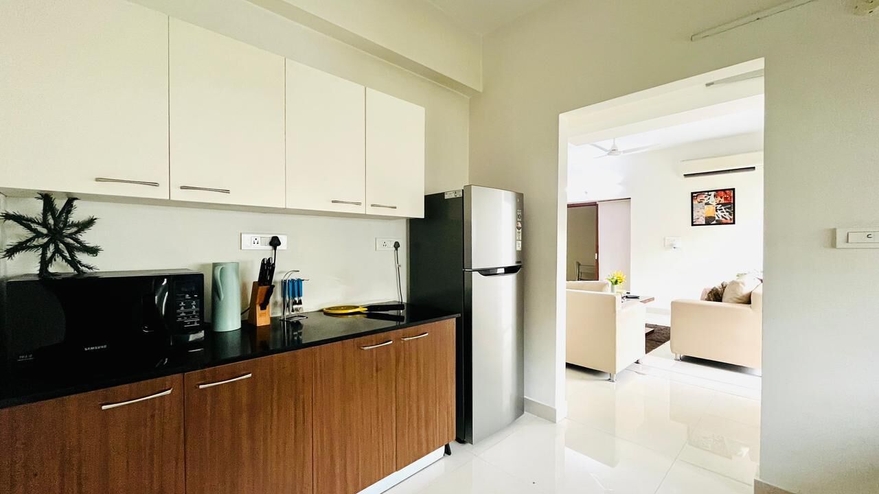 A modern kitchen with white cabinets, a black refrigerator, and a wooden countertop.