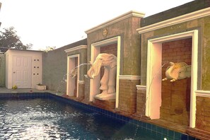Una piscina con un muro de ladrillo y tres estatuas de elefantes.