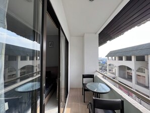 A balcony with a glass door, two small round tables, and a chair. - Emerald Hotel Jomtien (Pattaya)