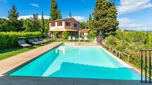 A swimming pool with lounge chairs, a wooden deck, and a house in the background. - Vacation home Lilia by Interhome (Riparbella)
