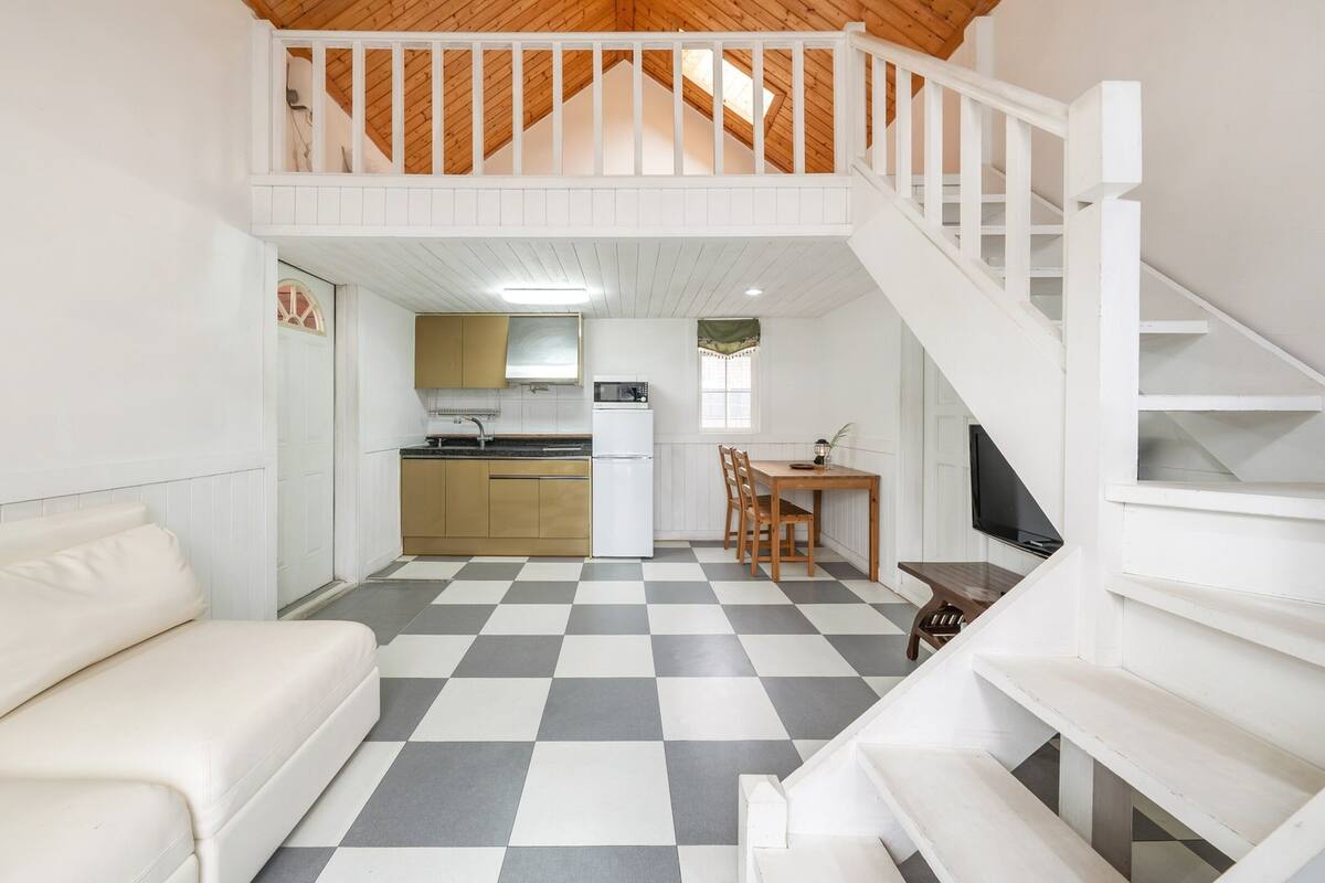 Ein kompakter Wohnraum mit Küchenzeile, Essbereich und einer Treppe, die in ein Obergeschoss führt.