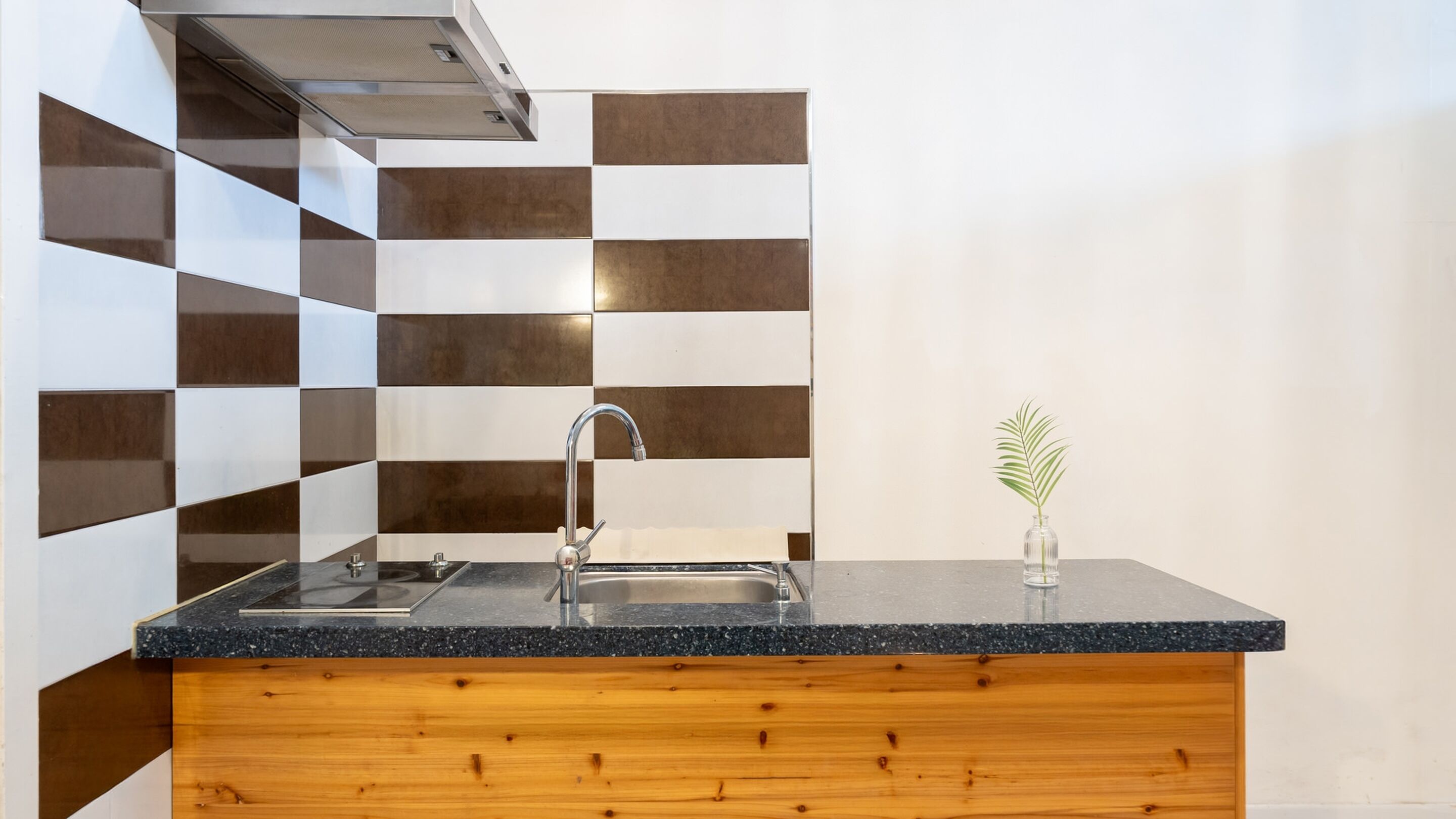 A kitchen with a black granite countertop, stainless steel sink, and a wooden base.