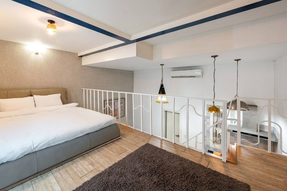 Ein modernes Schlafzimmer mit einem großen Bett, Holzboden, weißer Geländer und Blick auf die Küche.