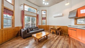 A cozy room with a wooden floor, a leather sofa, a wooden table, and a kitchen area with orange cabinets. - Gapyeong Solle Spa Pension (Gapyeong)