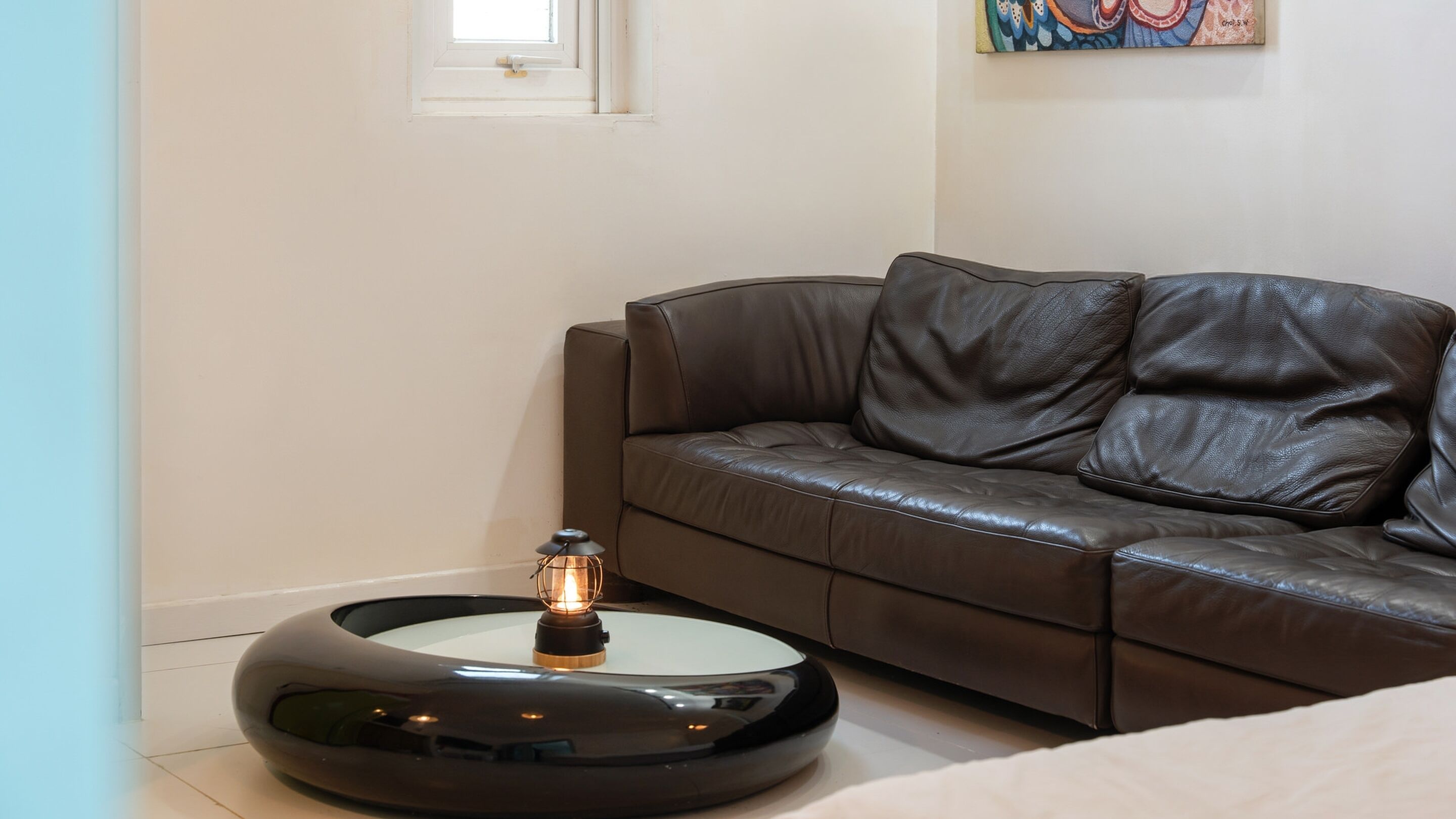 Un salon moderne avec un canapé en cuir marron, une table basse ronde noire et une petite lampe de table.