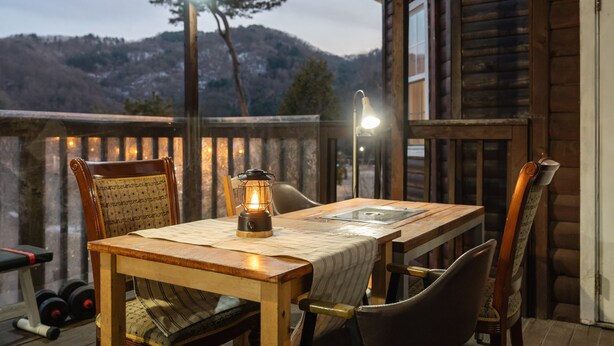A wooden table with a lantern on it, surrounded by chairs, on a balcony with a view of mountains. - Gapyeong Solle Spa Pension (Gapyeong)