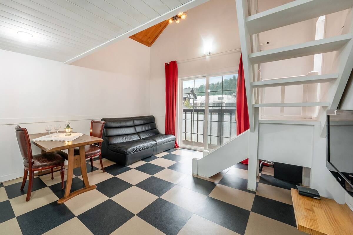 Ein Zimmer mit Schachbrettboden, einem schwarzen Ledersofa, einem Holzespeisesaal mit zwei Stühlen und einer Treppe mit weißer Geländer.