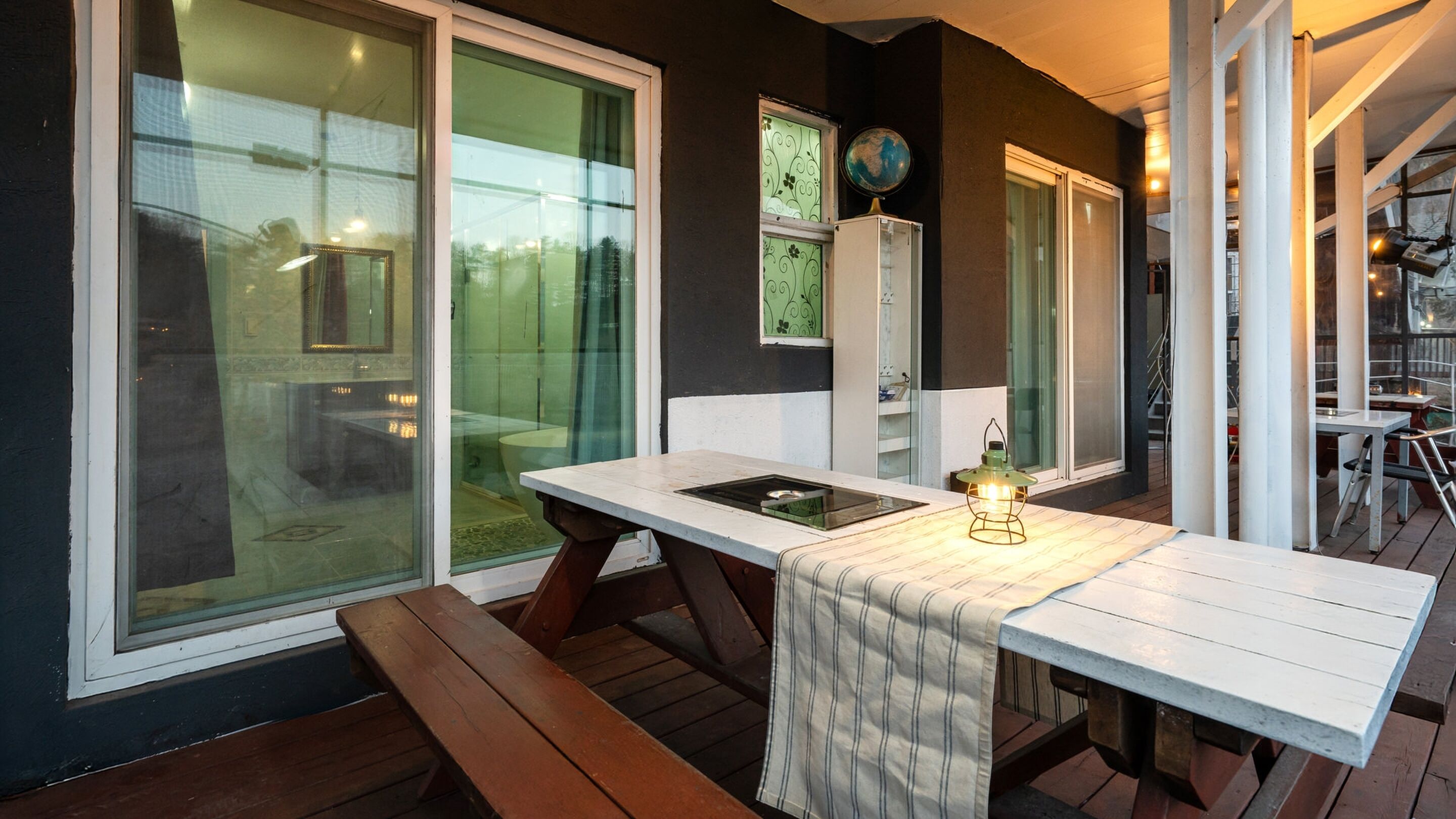 An outdoor dining area with a white table and benches, surrounded by glass doors and windows.