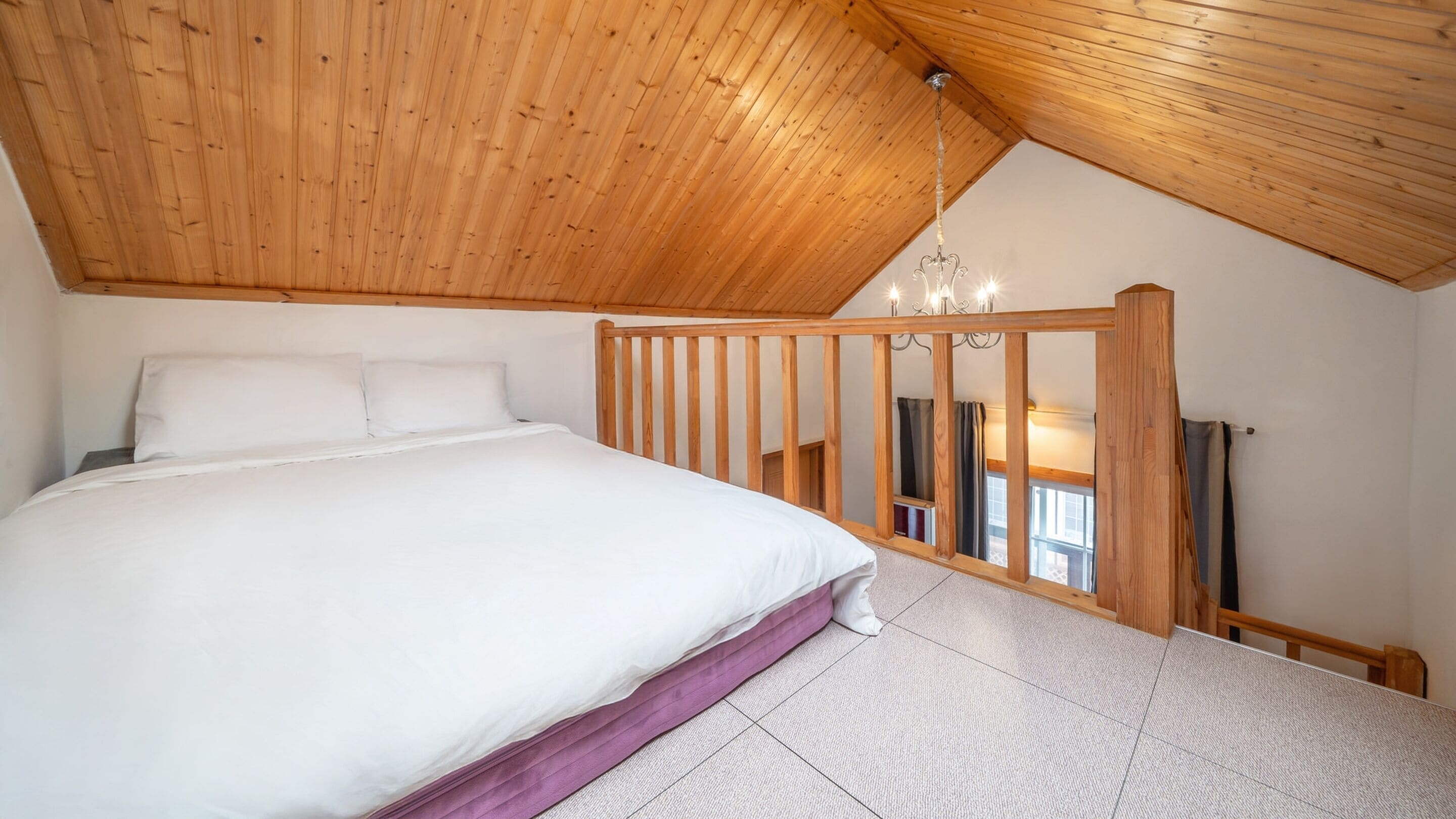 Une chambre avec un plafond en bois, un lit avec une literie blanche et une vue sur un balcon doté d’une balustrade en bois.