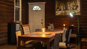 L’intérieur d’un chalet en bois, avec une table à manger, des chaises, une lampe et un tableau encadré accroché au mur.