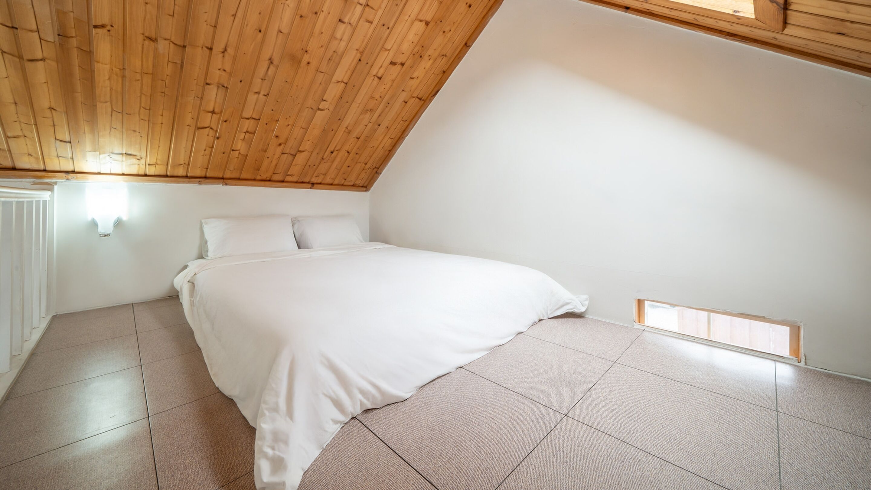 Une chambre avec un plafond en pente, un grand lit et une petite fenêtre.