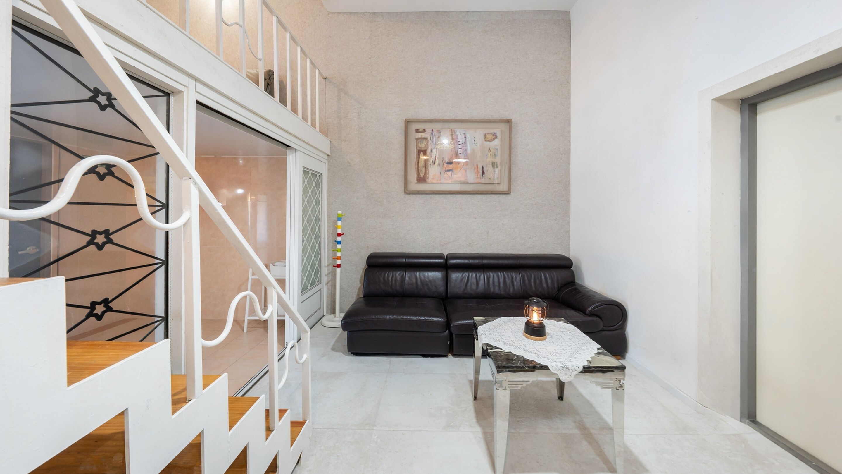 A modern living room with a black leather sofa, a small table with a candle, and a staircase with white railings.