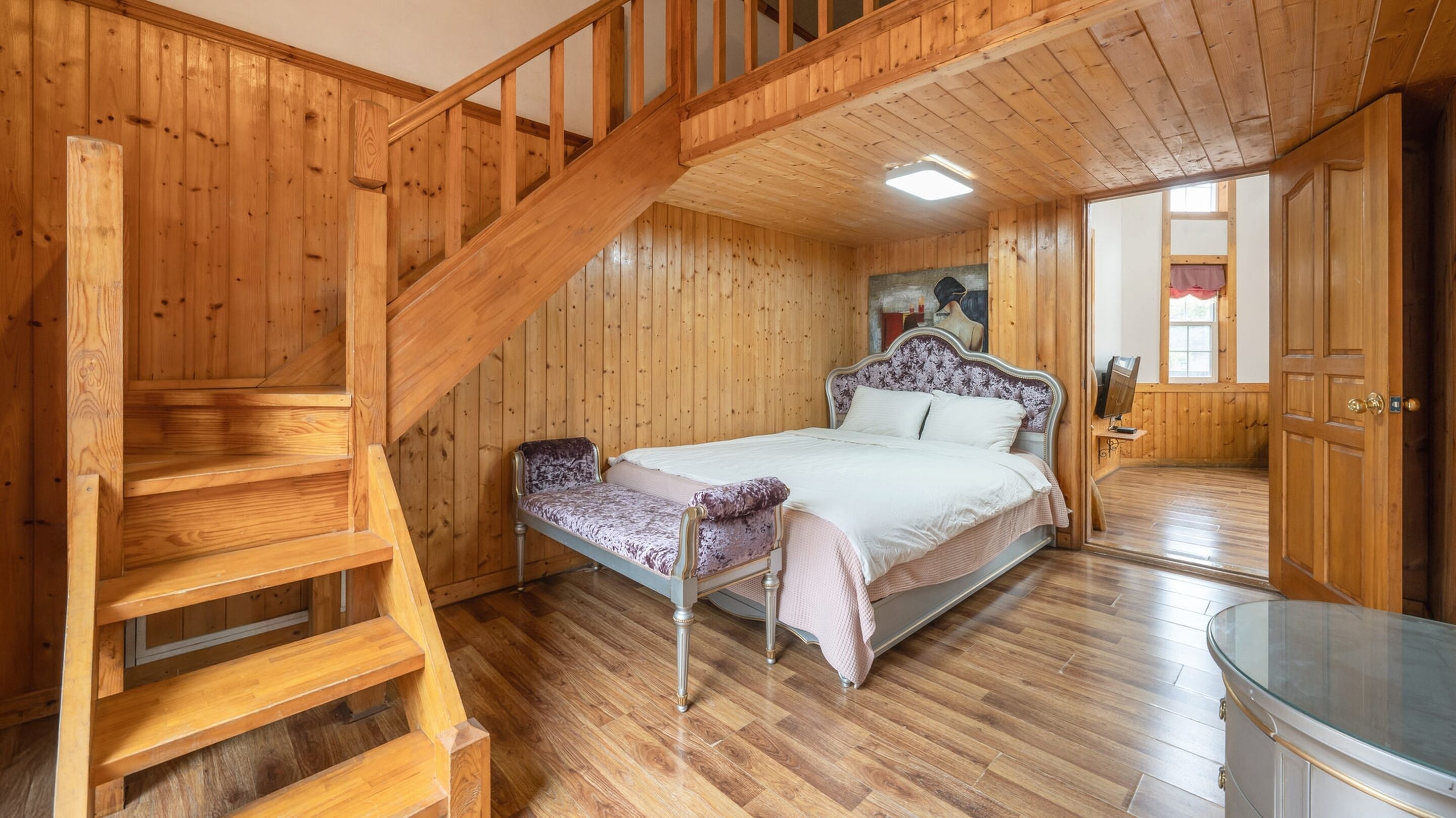 A wooden interior with a bed, a staircase, and a glass table.