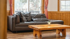 A cozy living room with a leather sofa, wooden coffee table, and a view through a window with curtains. - Gapyeong Solle Spa Pension (Gapyeong)