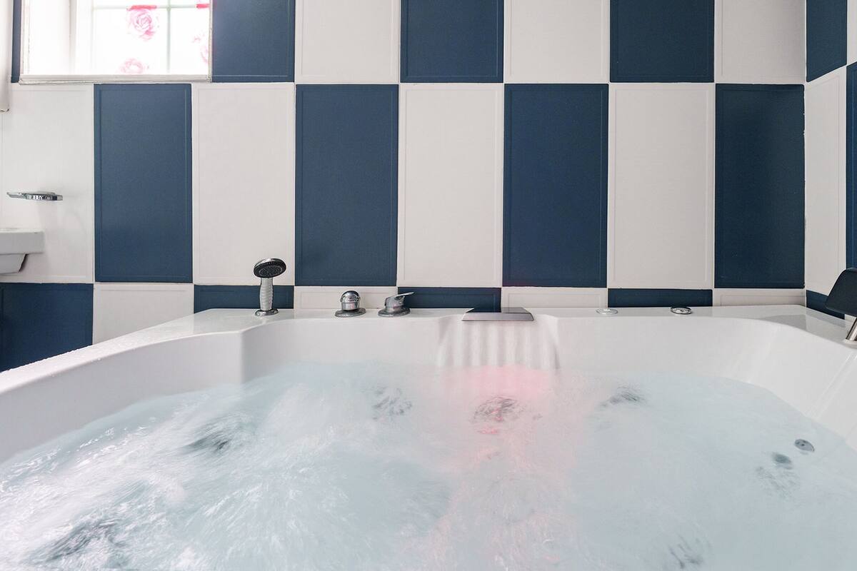 Ein Badezimmer mit einer mit Wasser gefüllten Badewanne, einem Waschbecken und einem Fenster mit Blick auf rosa Blüten.