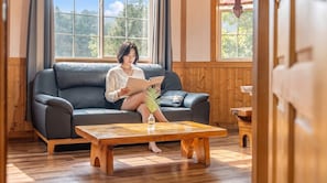 A person sitting on a dark leather sofa in a room with wooden walls and floors, reading a book titled 'KINELIK'. - Gapyeong Solle Spa Pension (Gapyeong)