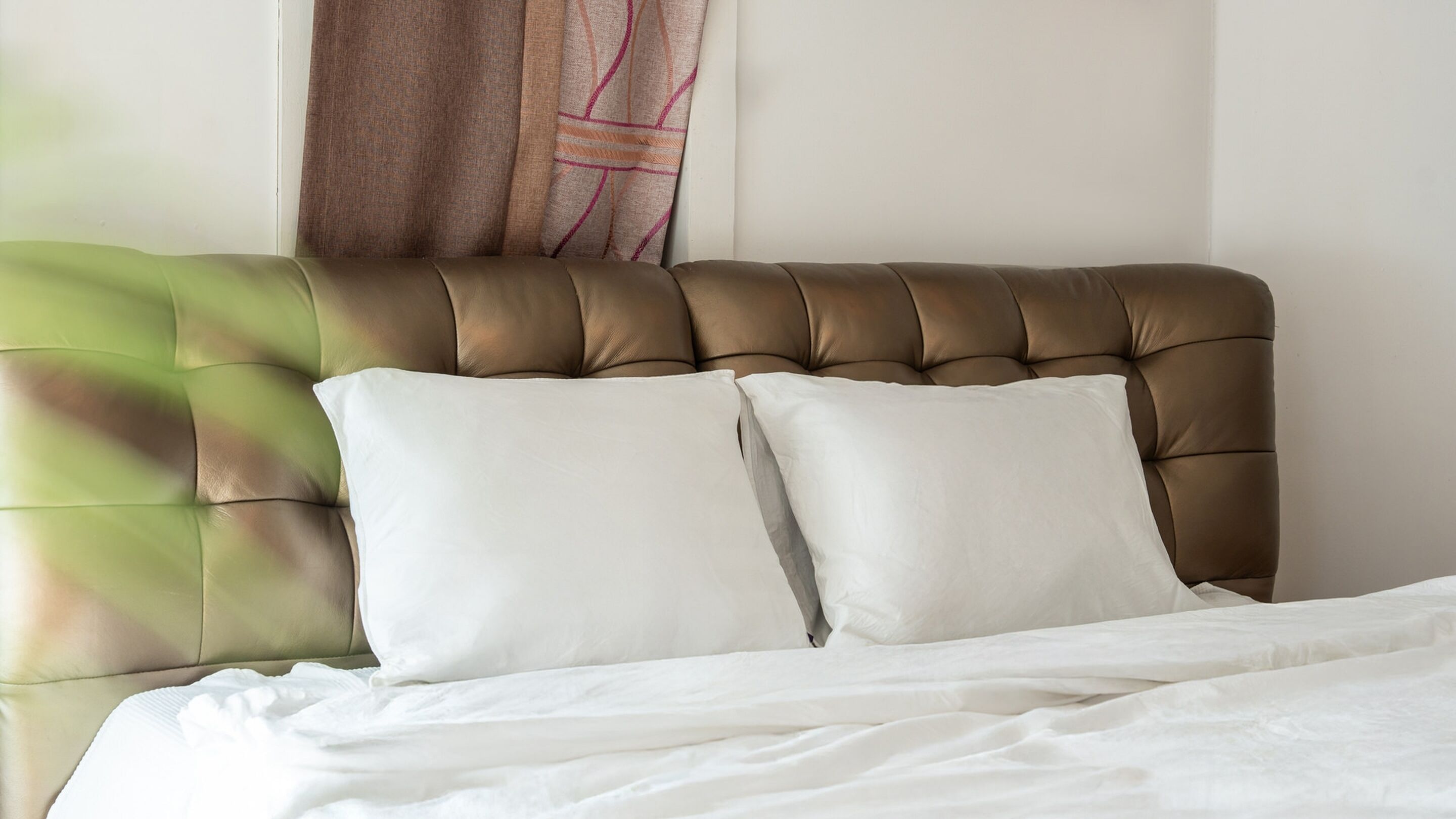 Una cama con cabecera capitonada, dos almohadas blancas y un edredón blanco.