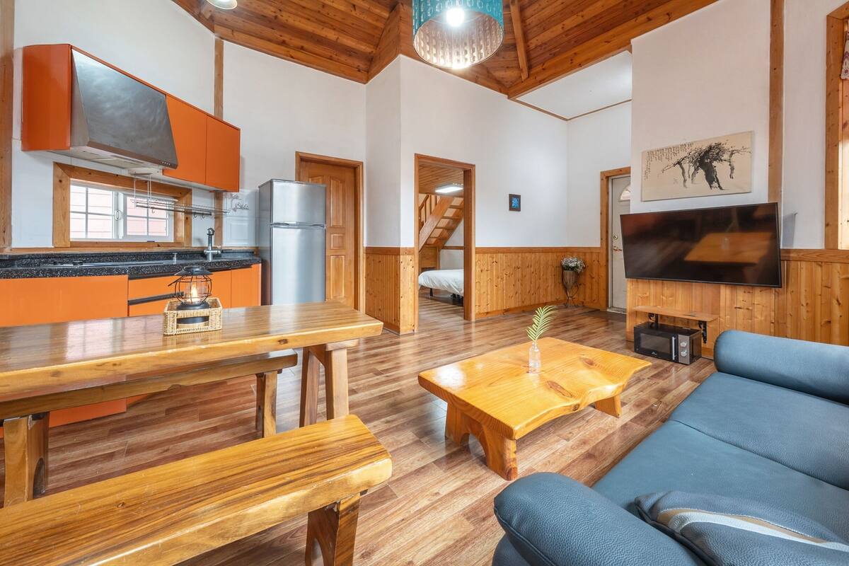 Ein gemütliches Wohnzimmer mit einem Holzesstisch, einer Couch und einem an der Wand befestigten Fernseher.