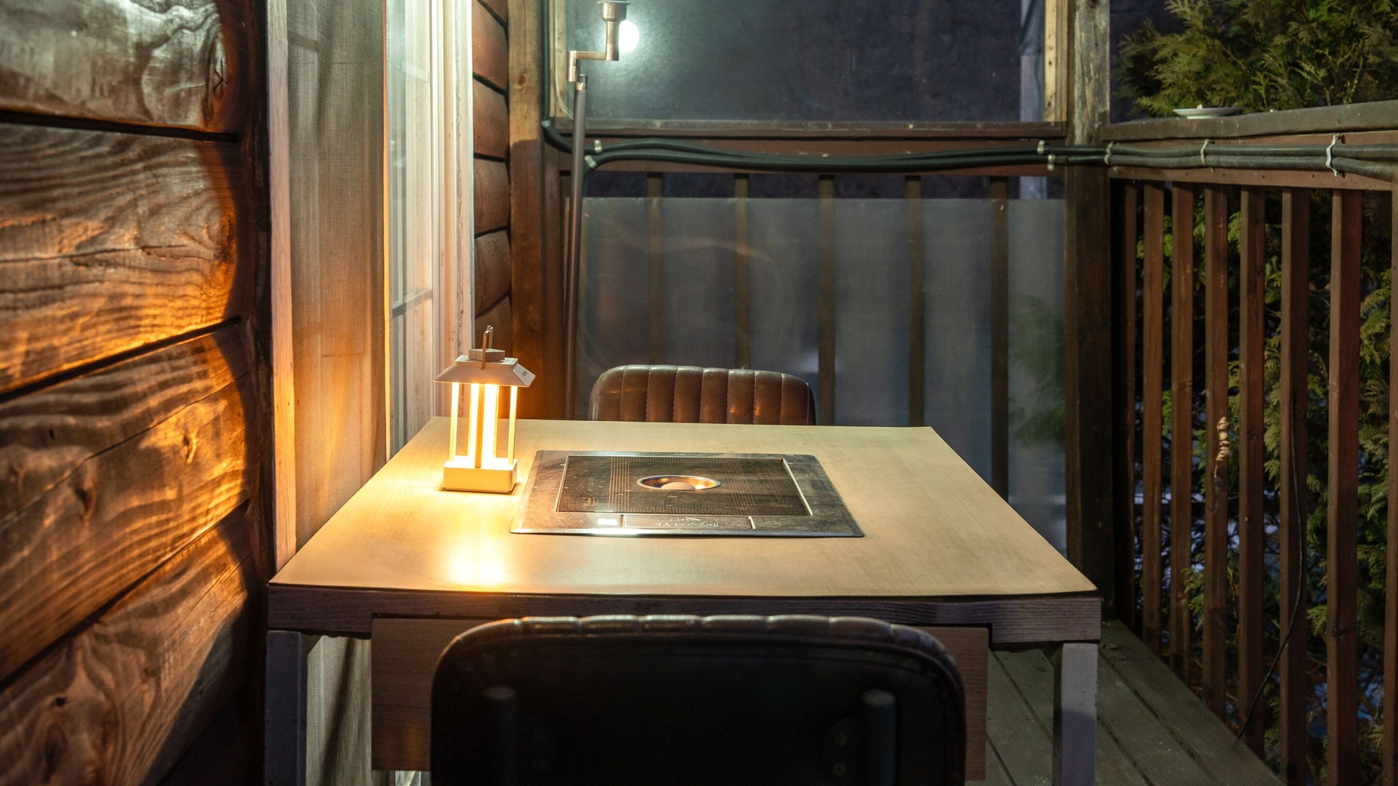 A wooden deck with a table and chairs, a lantern, and a metal railing.