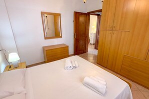 A bedroom with a bed, a wooden wardrobe, a bedside table with a lamp, and a mirror on the wall.