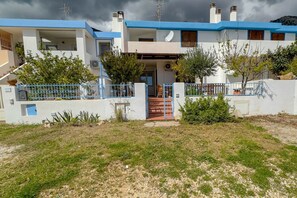 Una casa de dos pisos con fachada azul y blanca, una escalera visible y un patio delantero cercado.