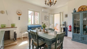 A dining area with a table set for four, chairs, a chandelier, a blue cabinet with glass doors, and a fire extinguisher on the wall.