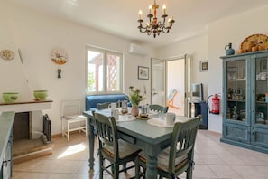 Un coin repas avec une table dressée pour quatre personnes, des chaises, un lustre, un buffet bleu aux portes vitrées et un extincteur fixé au mur.