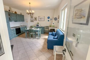 A compact kitchen with teal cabinets, a dining area with a table and chairs, a blue sofa, and a chandelier.