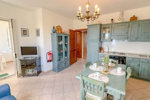 A kitchen with teal cabinets, a dining table with chairs, a chandelier, and a television on a stand.