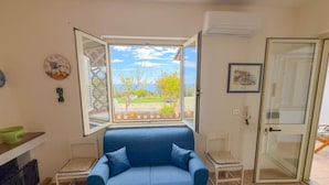 A room with a blue sofa, a window with a view, a door, and a wall clock.