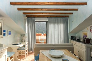 A room with a dining table, a sofa, a TV, and a window with curtains.